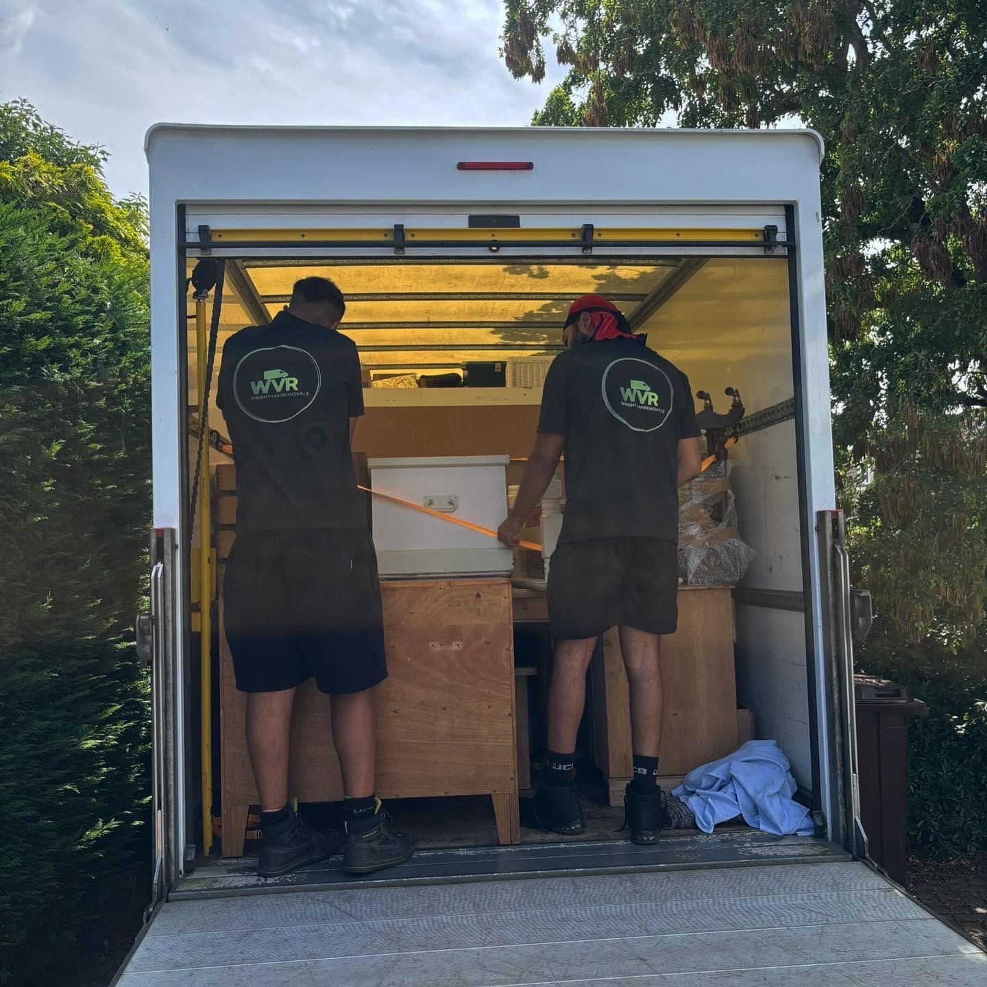Two WrightVanRemovals crew members strapping a crate inside a Luton van